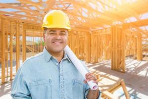 empreiteiro masculino hispânico com planos de projeto usando capacete no canteiro de obras foto