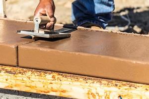 trabalhador da construção civil usando sulcador de mão em cimento úmido formando coping em torno de uma nova piscina foto