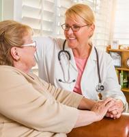 médico ou enfermeira sorridente feliz conversando com uma mulher sênior na cadeira em casa foto