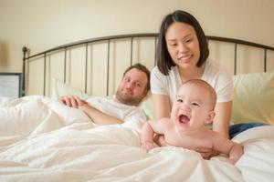 menino chinês e caucasiano deitado na cama com seus pais foto