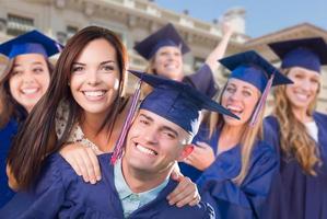 graduado masculino orgulhoso em boné e vestido com menina entre outros graduados atrás foto