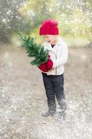 menina em luvas segurando pequena árvore de natal com efeito de neve foto