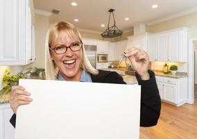 jovem mulher segurando placa em branco e chaves dentro da cozinha foto