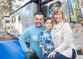 feliz família jovem de raça mista na frente de seu lindo trailer no acampamento. foto