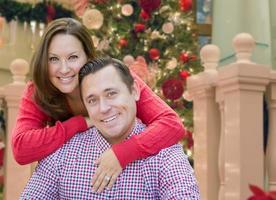 casal caucasiano abraçando na frente da árvore de natal decorada. foto