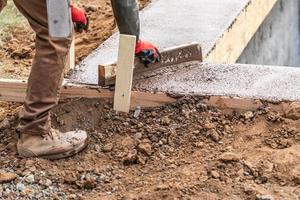 trabalhador da construção civil nivelando cimento molhado em moldura de madeira foto