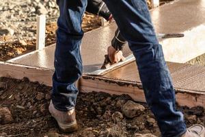 trabalhador da construção civil usando espátula de madeira em cimento úmido formando coping ao redor da nova piscina foto