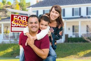 família de raça mista feliz na frente de casa e vendida para venda sinal imobiliário foto