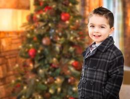 bonito menino caucasiano e hispânico de raça mista na frente da árvore de natal. foto