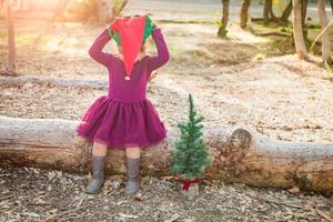 menina bonita de raça mista se divertindo com chapéu de natal e árvore ao ar livre foto