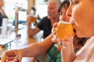 mulher bebendo copo de cerveja micro brew no bar com amigos foto