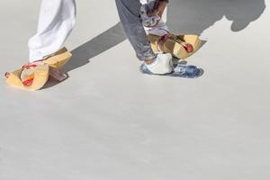 trabalhador usando esponjas em sapatos alisando reboco de piscina molhada com espátula foto