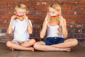 bonito jovem cuacasiano e menina comendo melancia contra a parede de tijolos foto