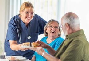 médica ou enfermeira servindo sanduíches de casal adulto sênior na mesa foto