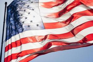 bandeira americana retroiluminada balançando ao vento contra um céu azul profundo foto