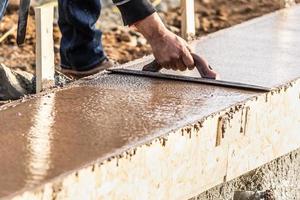 trabalhador da construção civil usando espátula de madeira em cimento úmido formando coping ao redor da nova piscina foto