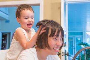 menino chinês e caucasiano de raça mista feliz se divertindo com a mãe chinesa dentro de casa foto