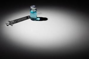 agulha de seringa e frasco de medicamento com ponto químico azul claro iluminado em fundo reflexivo foto