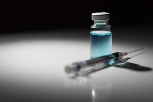 agulha de seringa e frasco de medicamento com ponto químico azul claro iluminado em fundo reflexivo foto
