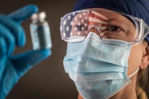 bandeira americana refletindo na trabalhadora médica segurando o frasco de vacina usando óculos e máscara facial protetora foto