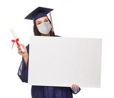 mulher graduada usando máscara facial médica e boné e vestido segurando cartolina em branco isolada em um fundo branco foto