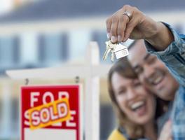 casal de raça mista em frente a placa de imóveis vendidos e casa com chaves foto