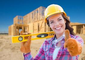 trabalhador da construção civil feminino com polegares para cima segurando nível usando luvas, capacete e óculos de proteção no canteiro de obras foto