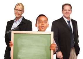 menino hispânico segurando placa de giz com professores atrás foto
