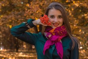 menina com um lenço no pescoço segura raminho de sorveira e sorri foto