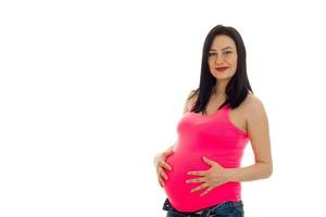 linda garota grávida em uma camiseta brilhante mantém as mãos atrás do estômago isoladas no fundo branco foto