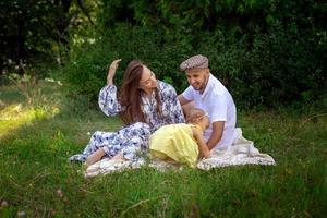 família jovem feliz brinca com sua filhinha no prado verde foto