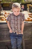 menino frustrado na fazenda de canteiro de abóboras em pé contra a carroça de madeira foto
