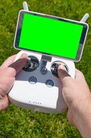 mãos segurando o controlador drone quadcopter com tela verde em branco foto