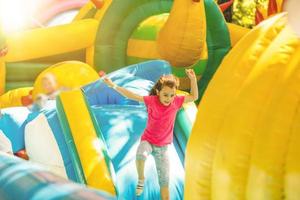 menina feliz se divertindo muito em um castelo de salto durante o deslizamento. foto