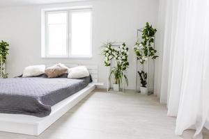 quarto claro com parede branca, cama grande com roupa de cama cinza e móveis feitos à mão