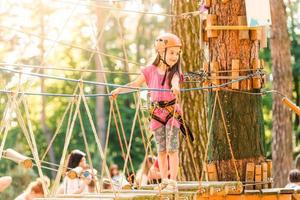 adorável menina aproveitando seu tempo na escalada do parque de aventura em um dia quente e ensolarado de verão. atividades de verão para crianças pequenas. criança se divertindo nas férias escolares. foto