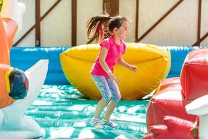 criança pulando na cama elástica colorida do playground. as crianças pulam no castelo de salto inflável na atividade da festa de aniversário do jardim de infância e brincam no centro para crianças pequenas. menina brincando ao ar livre no verão foto