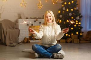 foto de moda de natal de uma linda garota com cabelos loiros em roupas aconchegantes, posando perto da árvore do ano novo com presentes