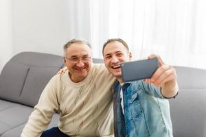 pai sênior com filho adulto relaxando no sofá em casa foto