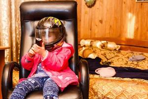 menina em um capacete de moto em uma cadeira em casa foto