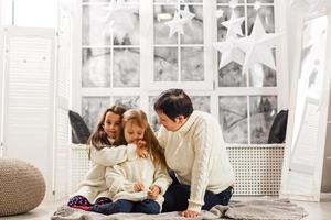 feliz natal e boas festas. mãe alegre e suas lindas filhas meninas trocando presentes. pai e dois filhos pequenos se divertindo e brincando juntos perto da árvore de natal dentro de casa. foto