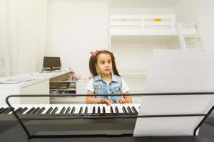 menina bonitinha toca piano, sintetizador. Treinamento. Educação. escola. formação estética. sala de aula elementar. foto