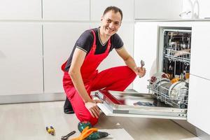 jovem técnico masculino consertando máquina de lavar louça na cozinha foto