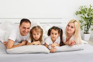 uma jovem família com filhos pequenos para a cama no quarto foto