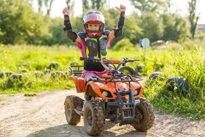 a menina anda de quadriciclo. uma mini moto-quatro é uma garota legal em um capacete e roupas de proteção. carro elétrico de quadriciclo elétrico para crianças populariza tecnologia verde foto