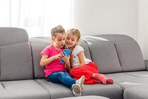 fique em casa fique seguro. duas crianças felizes sentadas na cadeira aconchegante relaxando brincando na sala branca dentro de casa. irmãs se divertindo em casa foto