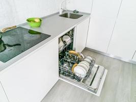 máquina de lavar louça aberta com pratos limpos na cozinha branca foto
