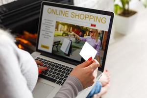 conceito de compras online. visão traseira da menina usando laptop, olhando para o site, segurando o cartão de crédito, sentado em casa foto