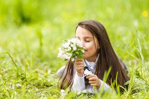 linda garotinha deitada no campo na grama verde e soprando dente de leão. ao ar livre. Aproveite a natureza. menina sorridente saudável no gramado da primavera. conceito livre de alergia. liberdade foto