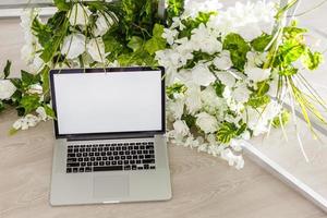 mesa de escritório em casa com laptop de tela em branco, lindas rosas e buquê de eucalipto, blog, site ou conceito de mídia social foto